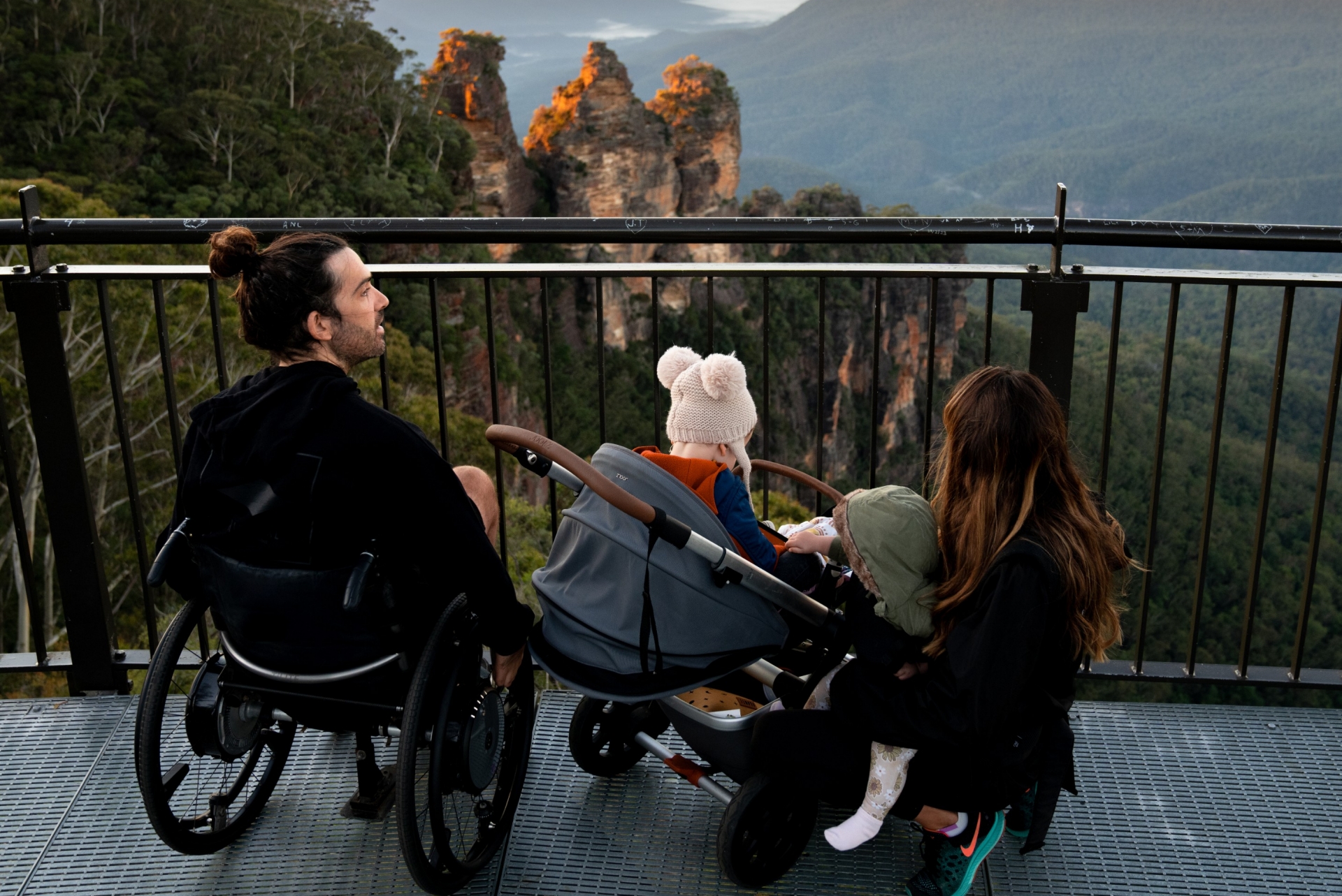 Ein Mann in einem Rollstuhl mit seiner Familie, die auf die Three Sisters in den Blue Mountains schauen, New South Wales © Tourism Australia