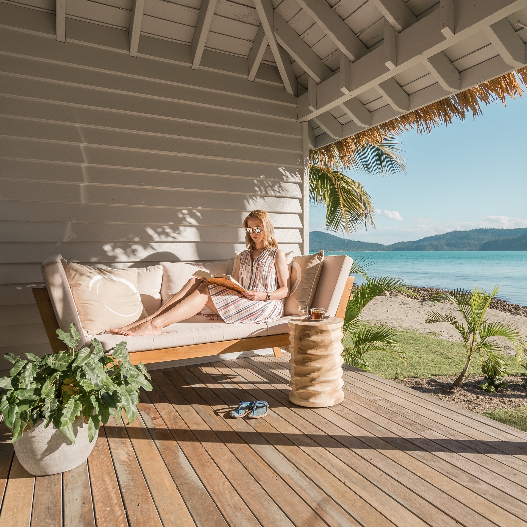 Eine Frau liest ein Buch auf einem Balkon am Meer im Elysian Retreat © Elysian Retreat/Nathan White