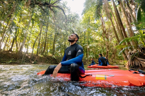 Ein Mann sitzt auf einem schwimmenden Floß in einem Fluss und blickt auf das grüne Blätterdach des Regenwaldes mit Back Country Bliss Adventure im Daintree Rainforest, Queensland © Tourism Australia