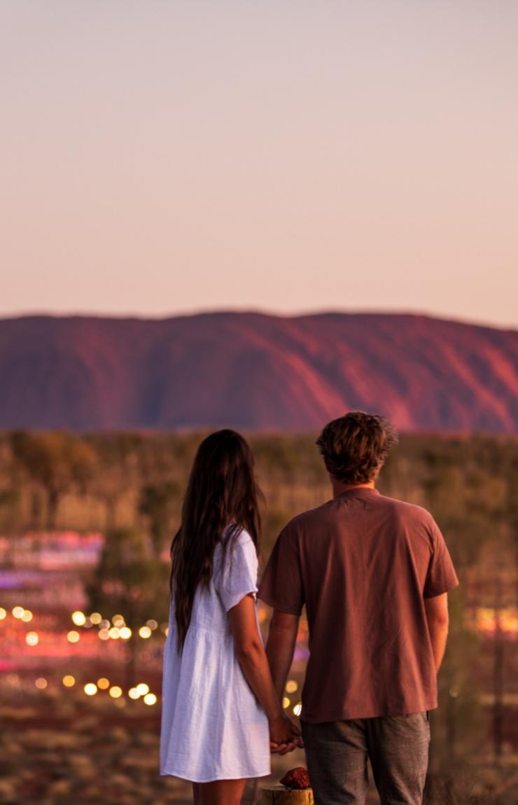 Ein Paar steht im Northern Territory bei Sonnenuntergang vor Uluru und dem Field of Light © Tourism NT/The Salty Travellers
