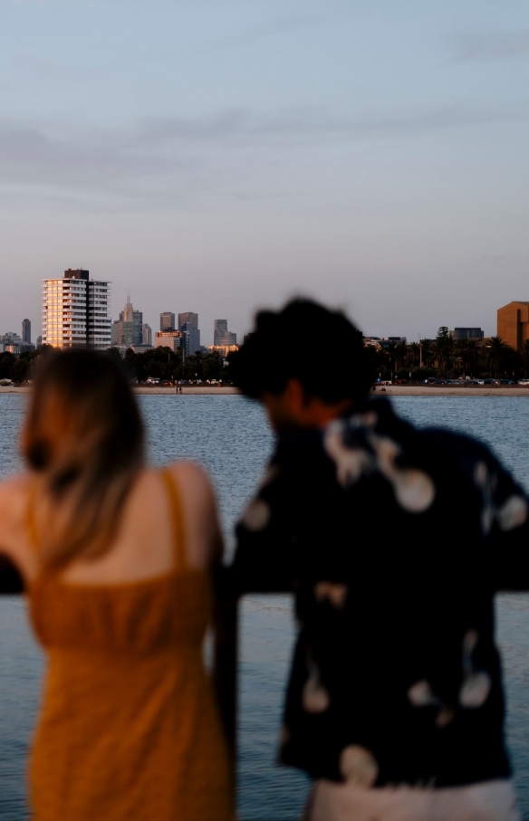 Ein Mann und eine Frau bewundern vom St Kilda Pier aus die Aussicht auf die in der Ferne liegende Stadt, Melbourne, Victoria © Visit Victoria