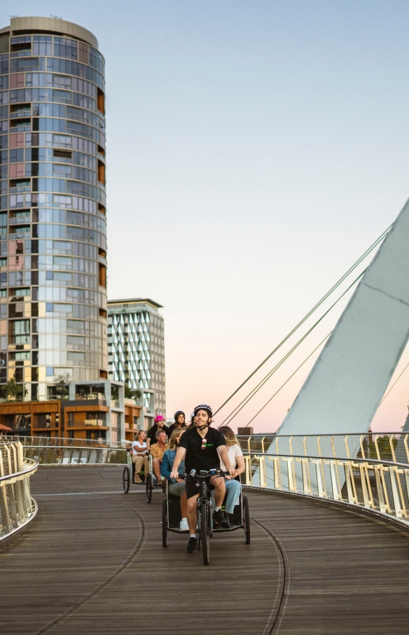 Eine Gruppe Touristen genießt eine nächtliche Rikscha-Taxifahrt über eine Brücke mit Peddle Perth, Perth, Westaustralien © Tourism Australia