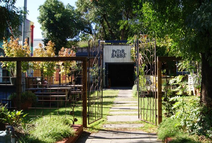 Iron gates open to a pathway through a lush green garden with picnic tables, leading to a building with a sign reading 'Peter Rabbit', Adelaide, South Australia © James McIntyre Iron gates open to a pathway through a lush green garden with picnic tables, leading to a building with a sign reading 'Peter Rabbit', Adelaide, South Australia © James McIntyre