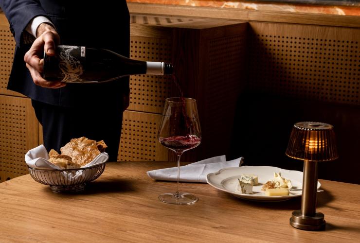 A waiter pouring a glass of red wine at a table set with a cheese plate and bread at Reine & La Rue, Melbourne, Victoria © Reine & La Rue