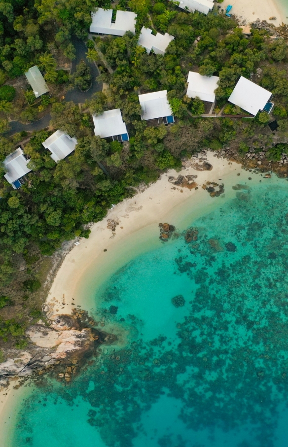 Aerial view over Lizard Island Resort accommodation amid the trees on the white sandy coastline of Lizard Island, leading to clear blue ocean in Queensland © Tourism and Events Queensland