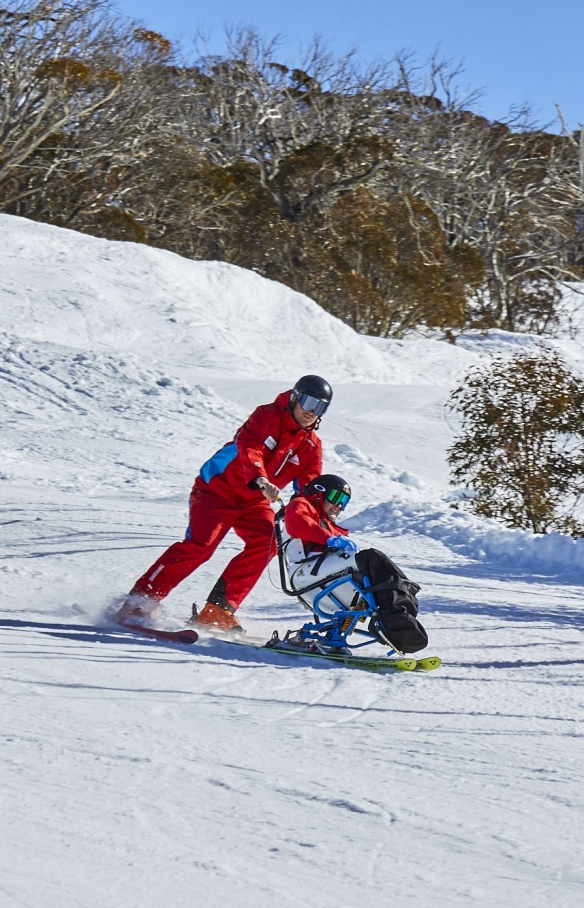 Two people with limited mobility adaptive skiing with instructors down a snow-covered mountain in Thredbo, Snowy Mountains, New South Wales © Tourism Australia