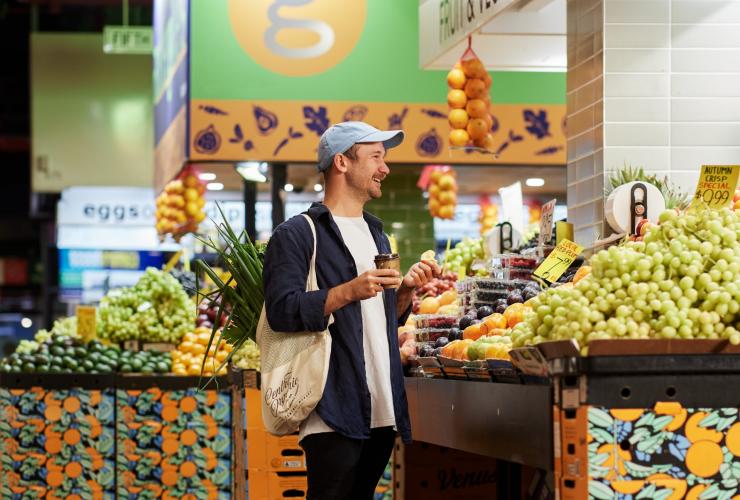 A person standing at a stall brimming with colourful fruit while holding a coffee at Adelaide Central Market, Adelaide, South Australia © South Australian Tourism Commission A person standing at a stall brimming with colourful fruit while holding a coffee at Adelaide Central Market, Adelaide, South Australia © South Australian Tourism Commission
