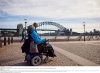 Person using a mobility device with another person walking beside them approaching the Sydney Opera House with the Sydney Harbour Bridge in the background in Sydney, New South Wales © Destination NSW