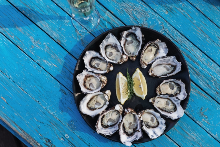 Aerial view over a plate of oysters spread out in a circle with lemon wedges in the centre on a blue table with Get Shucked, Bruny Island, Tasmania © Adam Gibson/Tourism Tasmania