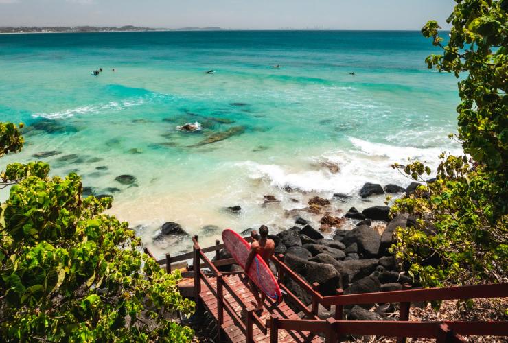 Man walking with surfboard at Rainbow Bay © Tourism and Events Queensland