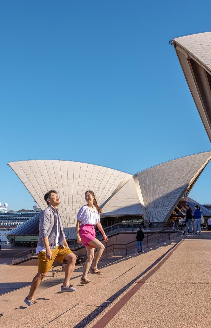 A couple walking along the forecourt in front of the Sydney Opera House, Sydney, New South Wales © Tourism Australia