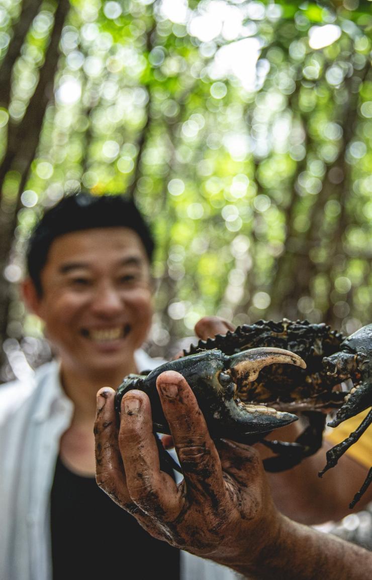 An Indigenous guide holding up a mud crab as a tour participant smiles widely behind him, Walkabout Cultural Adventures, Daintree Rainforest, Queensland © Tourism and Events Queensland An Indigenous guide holding up a mud crab as a tour participant smiles widely behind him, Walkabout Cultural Adventures, Daintree Rainforest, Queensland © Tourism and Events Queensland