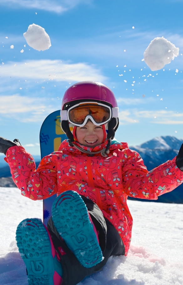 A child sitting on a snowy peak throwing snowballs in the air, Hotham Alpine Resort, Mt Hotham, Victoria © Hotham Alpine Resort