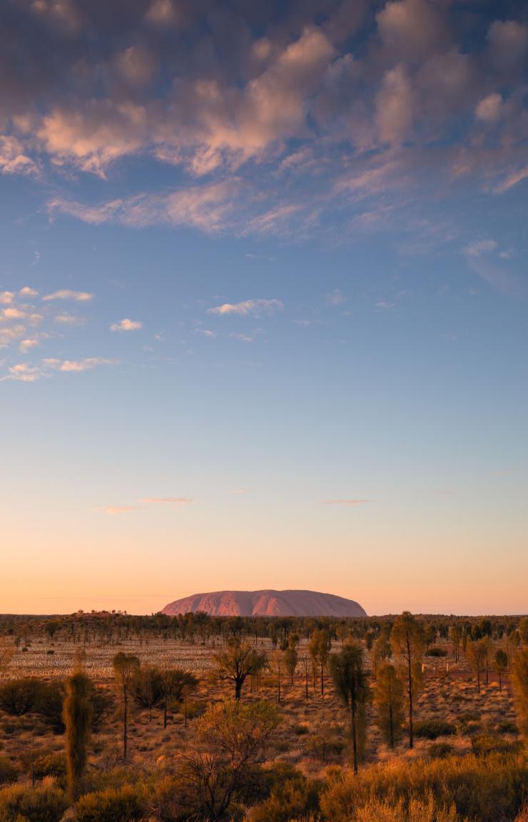 A large red rock monolith rising from the flat outback landscape at Uluru, Uluru-Kata Tjuta National Park, Northern Territory © Tourism Australia