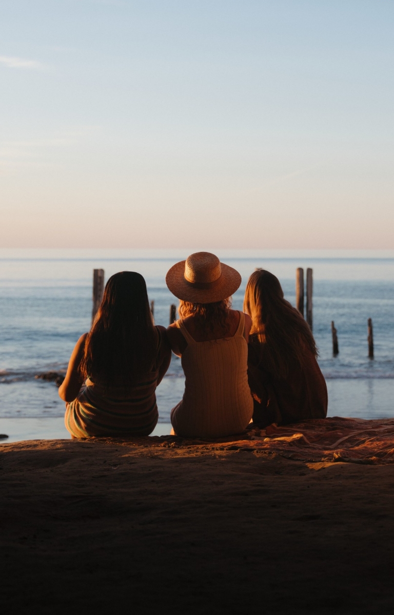 Three friends sitting together in a sandstone cave overlooking the ocean during sunset at Port Willunga Beach, Fleurieu Peninsula, South Australia © South Australian Tourism Commission