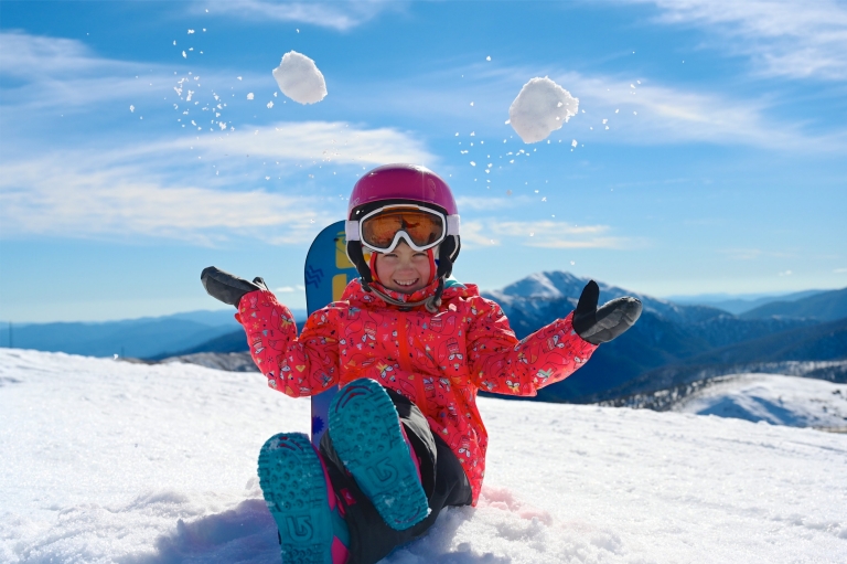 A child sitting on a snowy peak throwing snowballs in the air, Hotham Alpine Resort, Mt Hotham, Victoria © Hotham Alpine Resort