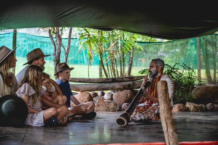 A family seated on the floor beside an Aboriginal guide wearing body paint and holding a didgeridoo at Rainforestation Nature Park, Kuranda, Queensland © Tourism and Events Queensland