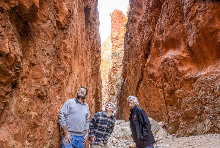 Homme en situation de handicap neurologique debout avec un guide et un autre homme admirant le Standley Chasm, West MacDonnell Ranges, Territoire du Nord © Tourism NT/Helen Orr