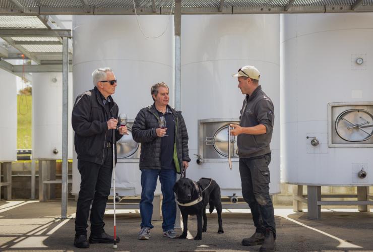 Homme avec un chien d'assistance en compagnie d'un ami et d'un guide au Puddleduck Vineyard, Richmond, Tasmanie © Dearna Bond