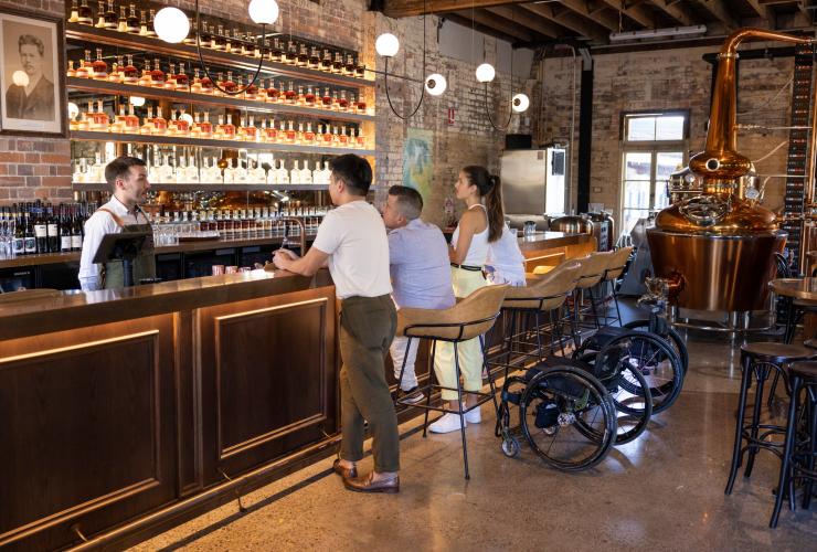 Amis assis au bar et faisant une dégustation de spiritueux dans le quartier de Rivermakers avec un fauteuil roulant près d'eux, Brisbane, Queensland © Tourism and Events Queensland