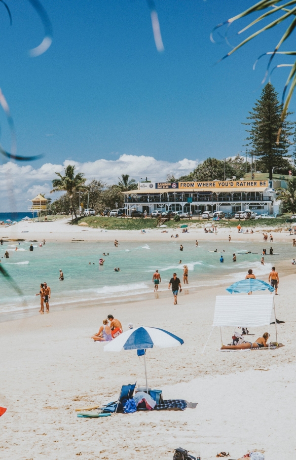 Personnes allongées sur le sable blanc sous des parasols colorés, tandis que d'autres nagent dans les vagues douces et les eaux cristallines de Greenmount Beach à Coolangatta, Queensland © Tourism and Events Queensland