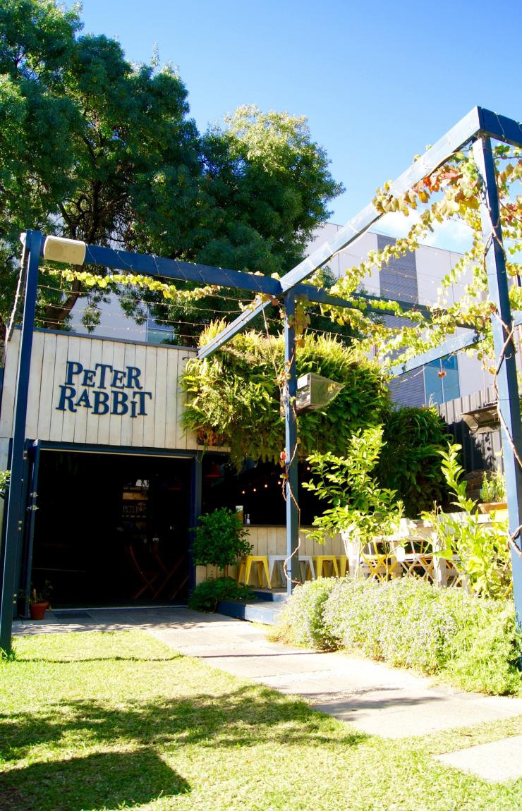 Sebuah taman yang rimbun dengan area tempat duduk outdoor di depan sebuah kafe dengan papan bertuliskan Peter Rabbit, Adelaide, South Australia © James McIntyre