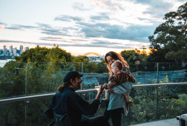 Seorang pria yang duduk di kursi roda bersama keluarganya menikmati pemandangan dari Taronga Zoo, Sydney, New South Wales © Tourism Australia