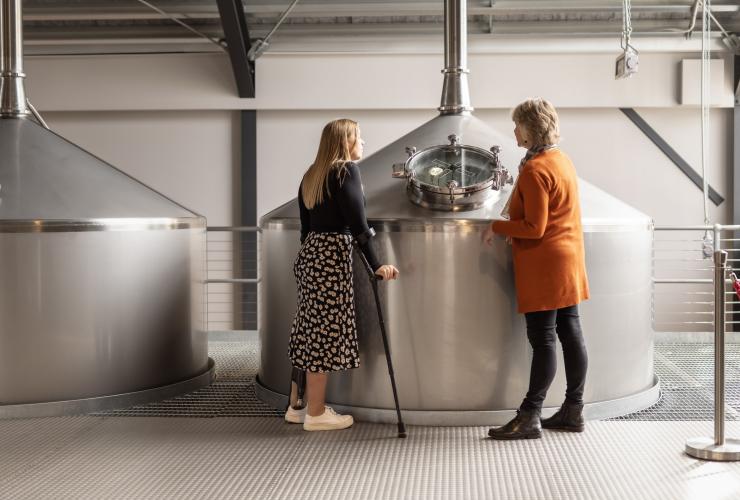Seorang wanita dengan alat bantu mobilitas berdiri bersama pemandu tur di Callington Mill Distillery, Oatlands, Tasmania © Dearna Bond