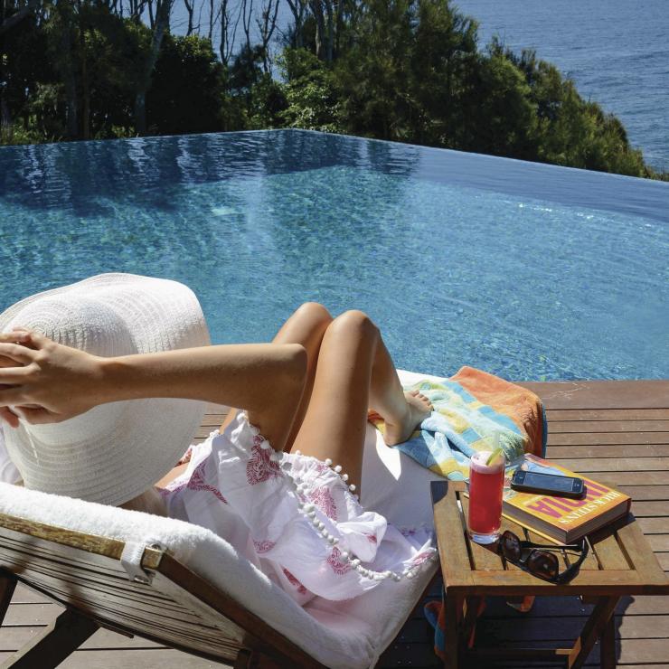 Wanita bersantai di tepi kolam renang tanpa batas dengan pemandangan samudra di Bannisters by the Sea, Mollymook Beach di South Coast. © Bannisters Hotel