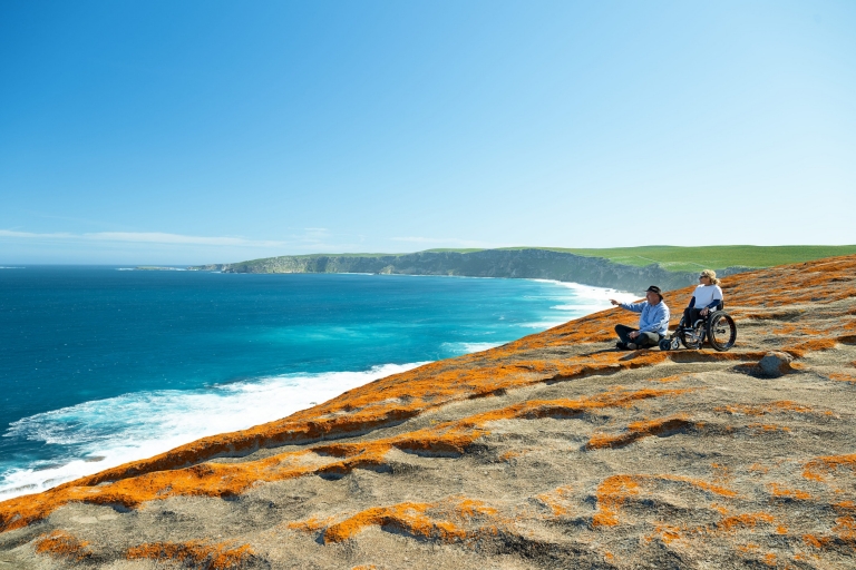 Seorang wanita di kursi roda dengan pemandu wisata yang menunjuk ke arah samudra biru Kangaroo Island, South Australia © Tourism Australia