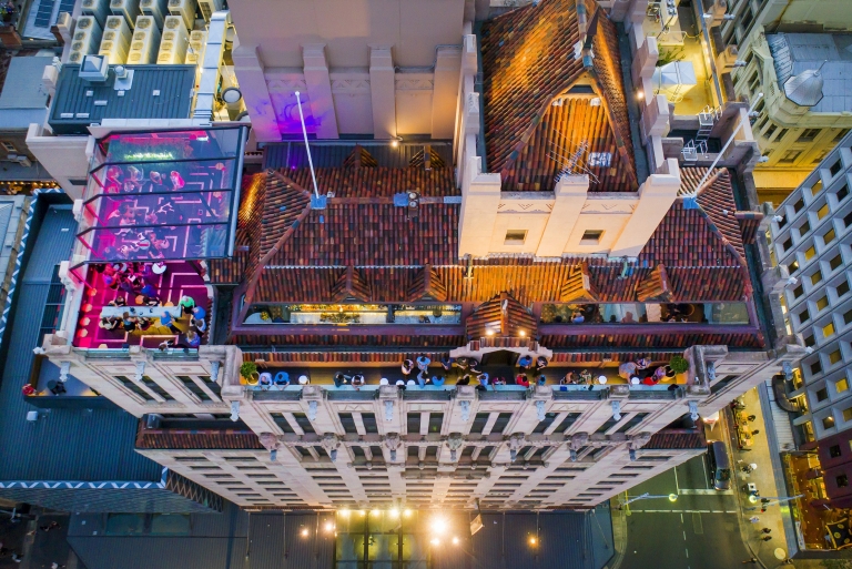 Veduta aerea dell'Hennessy Rooftop Bar del Mayfair Hotel, illuminato da lampade rosa e affollato di persone che sorseggiano un drink, Adelaide, South Australia © Mayfair Hotel