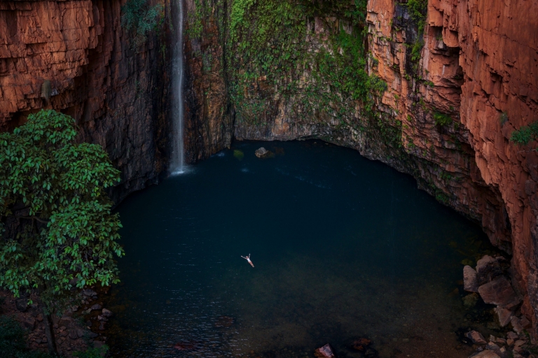 Vista aerea di una persona che galleggia sulla schiena in una sorgente di acqua blu circondata da imponenti pareti di roccia rossa ricoperte di muschio e una piccola cascata a Emma Gorge, El Questro Wilderness Park, Kimberley, Western Australia © Tourism Australia Vista aerea di una persona che galleggia sulla schiena in una sorgente di acqua blu circondata da imponenti pareti di roccia rossa ricoperte di muschio e una piccola cascata a Emma Gorge, El Questro Wilderness Park, Kimberley, Western Australia © Tourism Australia
