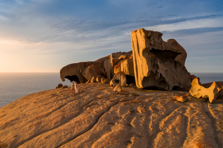 Due persone che camminano accanto alle grandi formazioni di Remarkable Rocks al tramonto con l'oceano sullo sfondo a Kangaroo Island, South Australia © South Australian Tourism Commission Due persone che camminano accanto alle grandi formazioni di Remarkable Rocks al tramonto con l'oceano sullo sfondo a Kangaroo Island, South Australia © South Australian Tourism Commission