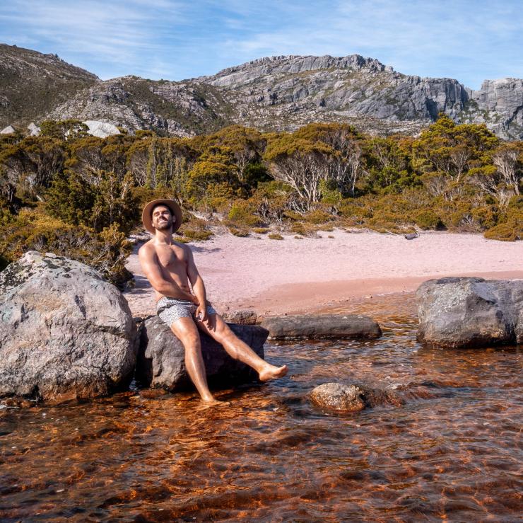 タスマニア州のウエスト・コーストの湖岸の岩の上でポーズを取るマイルズ・グレイ © Miles Gray, @milesuncharted