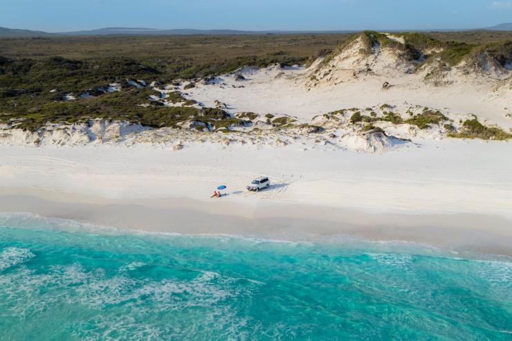 ケープ・ル・グラン国立公園のビーチに停めた4WDの横で日光浴を楽しむカップル © Australia's Golden Outback