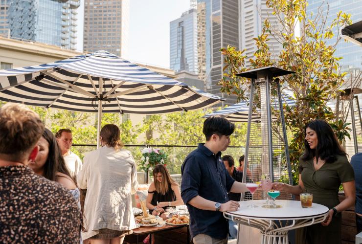 Groups of people enjoying cocktails on a sunny day beneath a sprinkling of umbrellas on the rooftop bar of the Imperial Hotel, East End, Victoria © Jesse Hisco/Visit Victoria