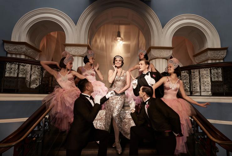 A group of people dressed in 1920s attire with one woman standing in the centre and smiling as others dote on her during OA Presents Opera The Merry Widow at Sydney Opera House, New South Wales © Georges Antoni