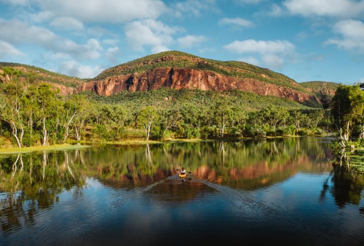 A person kayaking on still water surrounded by trees and rocky mountains on a sunny day at Mt. Mulligan Lodge, Mount Mulligan, Queensland © Mount Mulligan Lodge