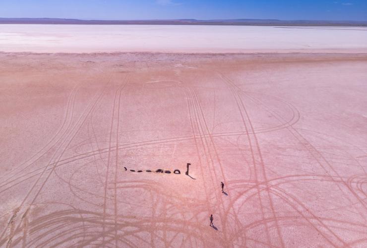 Aerial view of people standing beside a sea monster statue on the dried pink ground of Lake Bumbunga, Clare Valley, South Australia © Karen Smith