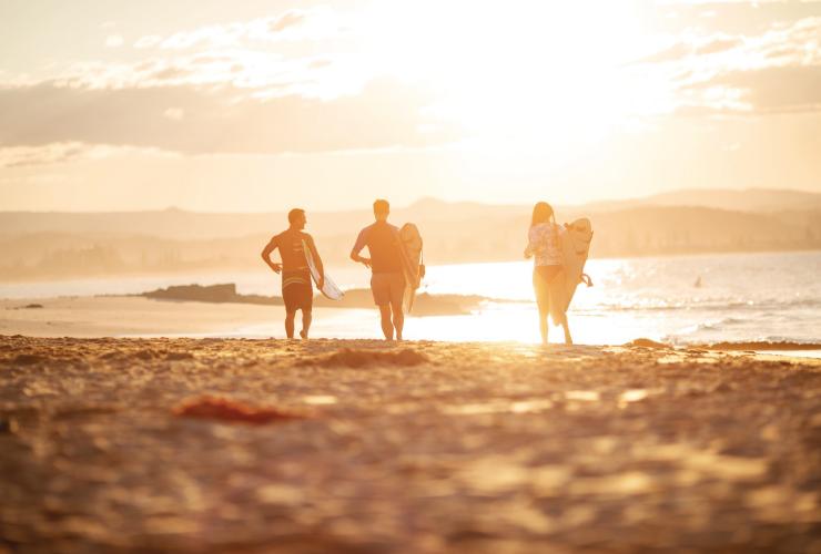 Three surfers are silhouetted by the sunrise as they run across the sand toward the ocean at Snapper Rocks, Gold Coast, Queensland © Tourism and Events Queensland