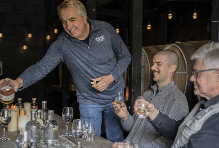 Staff member serving alcoholic spirits to smiling guests sitting at a table in McHenry Distillery, Tasman Peninsula, Tasmania © Tourism Australia