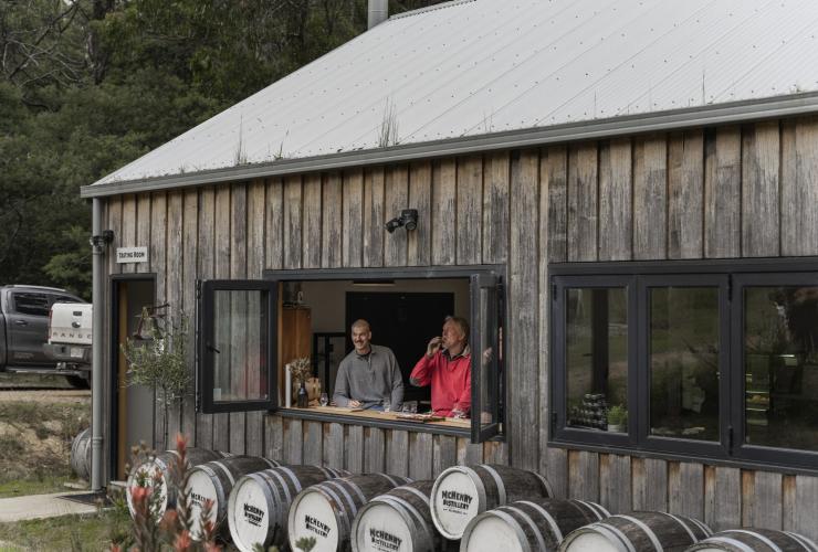 A small rustic building with two men sitting in the window looking out as they sip drinks at McHenry Distillery, Tasman Peninsula, Tasmania © Tourism Australia