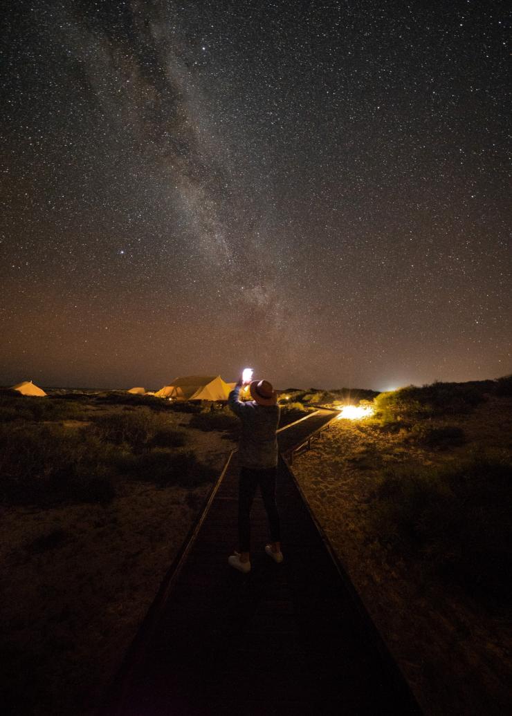 Person standing on a boardwalk taking a photo of the starry night sky as they approach Sal Salis, Ningaloo Reef, Western Australia © Sal Salis Ningaloo Reef