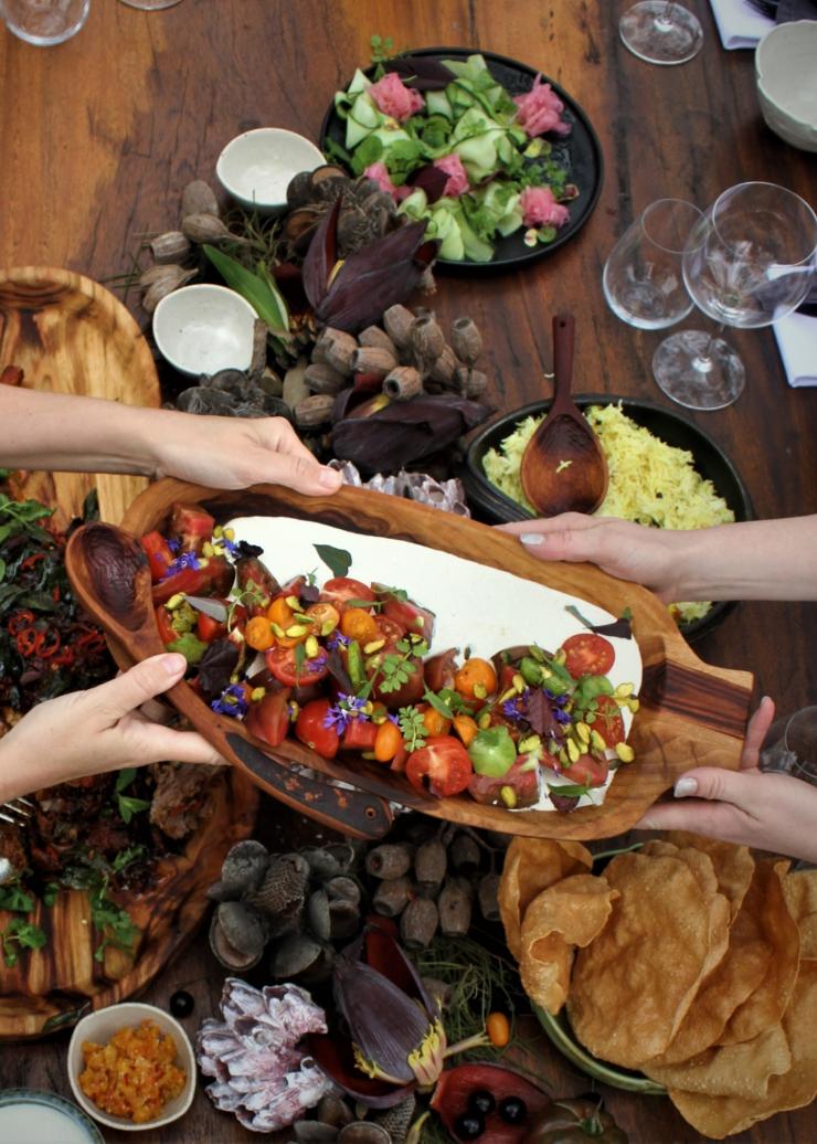 Aerial view over a table filled with food, with two people passing a dish across the frame Makepeace Island, Noosa, Queensland © Makepeace Island