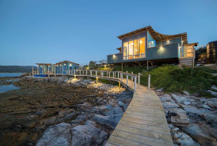 Close up on a pier over the calm ocean looking toward two buildings with large windows at night on Picnic Island,  Coles Bay, Freycinet, Tasmania © Picnic Island Pty Ltd