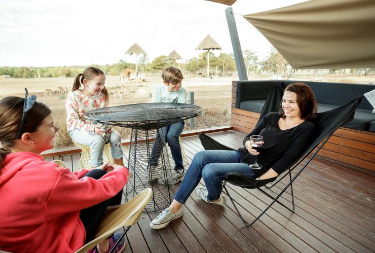 A family sitting on a balcony overlooking a giraffe enclosure at Taronga Western Plains Zoo, Dubbo, New South Wales © Destination NSW