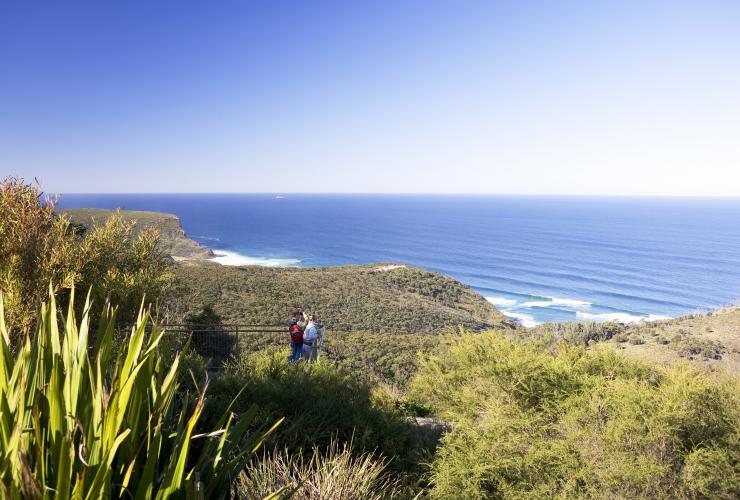 Due persone in piedi al Governor Game Lookout affacciate su un paesaggio ricco di vegetazione che va verso l'oceano al Royal National Park, Sydney, New South Wales © Destination NSW