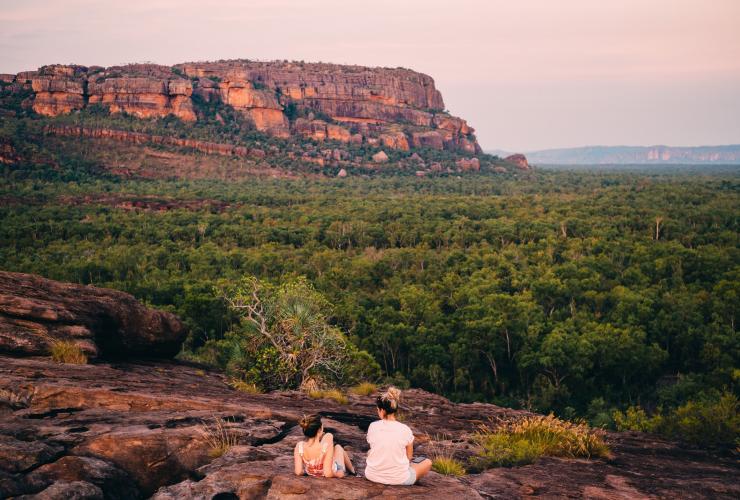 Due persone sedute su una scogliera rocciosa con vista sul vasto paesaggio ricco di vegetazione a Burrungkuy (Nourlangie) Rock, Kakadu National Park, Northern Territory © Tourism NT/Jewels Lynch