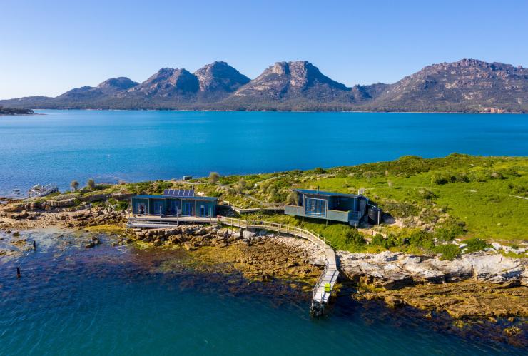 Vista sull'acqua verso due edifici e un molo sulla riva di Picnic Island, Coles Bay, Freycinet, Tasmania © Luke Tscharke