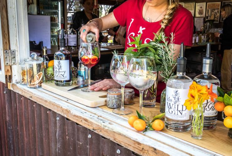 南澳州袋鼠島Kangaroo Island Spirits釀酒廠內調酒師在吧檯前倒出一杯含水果的雞尾酒的特寫鏡頭，吧檯上有新鮮水果、香草和一瓶杜松子酒©南澳州旅遊局